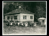 Hip roofed white school at Caretta with a group of children and adults in front. This picture is also found in the DeHaven Collection, Roll 1599 03.