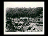 View of dam looking toward tunnel intake during the hydroelectric power construction on the New River. Excavation for dam shown in foreground, partially completed railway trestle over river at right and concrete mixer at left. New-Kanawha Power Company, Hawks Nest - Gauley Junction Development No. 141.