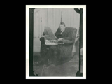 A man sitting in a rocking chair and holding a newspaper. Possibly Neuhardt's father.