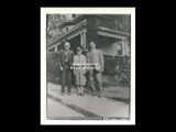 Three generations of the Neuhardt family standing on the sidewalk with a frame house in the background.