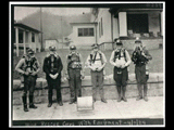 Six men with equipment (mine rescue corps) standing on the sidewalk in front of the clubhouse. This picture is also found in the DeHaven Collection, Roll 1602 03.