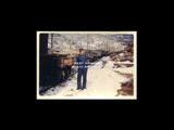 Man standing beside log train in winter. From small red photo album.