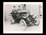 Two Wheeling policemen in automobile on brick street in front of building.