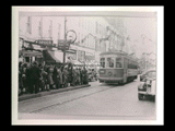 Car No. 59 streetcar, Wheeling-Benwood-McMechen line, approaching streetcar island stop on brick street. Signs include drugs, Hanover, SS Opticians.