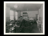 Interior view of a nurses classroom at Ohio Valley Hospital with wooden chair desks and a hospital bed at the far end.
