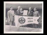 Green Cross Award of Honor. Five men standing behind microphones holding pennant and plaque.