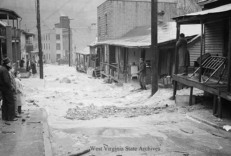 Many on-lookers view an inundated residential street leading down to a commercial area, Logan, 1939. Kenneth King Collection, West Virginia State Archives (336511)