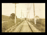 View down tracks of approaching streetcar at Edgemont. Rural setting with houses.