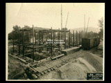 Girder structure on Building 2 (East Wing) during construction of the Cass Gilbert WV State Capitol building. A railroad track runs diagonally in the foreground with a car on it.