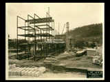 Girder structure on Building 2 (East Wing) during construction of the Cass Gilbert WV State Capitol building. Railroad cars and tracks are on the ground.