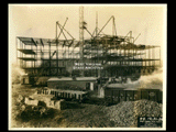 Girder structure on Building 2 (East Wing) during construction of the Cass Gilbert WV State Capitol building. Building 1 is visible behind the girder. Railroad cars are in the foreground.