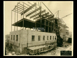 Ground level stonework on Building 2 (East Wing) during construction of the Cass Gilbert WV State Capitol building. Girder structure is visible. A railroad car is in the foreground.