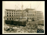 Fourth level stonework on Building 2 (East Wing) during construction of the Cass Gilbert WV State Capitol building. Railroad cars in the foreground. Light snow on the ground.