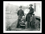 Man, woman, and three children wearing clothing for colder weather and standing alongside a frame house. Fence.