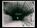 View into tunnel during the hydroelectric power construction on the New River. View shows shale roof supported by 6 inch H-beam ribs on 30 inch centers with 4x4 inch wooden lagging laid on lower flanges of H-beams. Excavation of invert completed except rounding the bottom. Camera at Station 13 + 40. New-Kanawha Power Company, Hawks Nest - Gauley Junction Development No. 315.