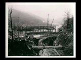 Power house during the hydroelectric power construction on the New River. View taken from top of portal cut showing superstructure steelwork completed. Bridge across the river in the distance. Opposite bank visible. New- Kanawha Power Company, Hawks Nest - Gauley Junction Development No. 342.