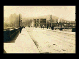 View across bridge toward Monongahela Valley Traction Company station at other buildings at Clarksburg. People on bridge. Sign for [Loar and] White Clarksburg Best Clothiers. Date (1-14-16) possibly 1917. Same as 0203 10.