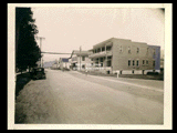 View down Main Street in Rainelle with parked automobiles. Bank of Rainelle (with Meadow River Lumber Company office) is first building on right side. Signs include Florsheim Shoe, Pioneer Hotel, Western Union, billiards, jewelry, drugs, and railroad crossing. (14) <p> Additional Note: Portion of photo appeared in the Rotogravure Edition of <i>The Greenbrier Independent</i> (November 22, 1929).