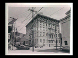 View across intersection of YMCA building in Wheeling. Automobiles moving on street. Signs for Top Value stamps, Pepsi.