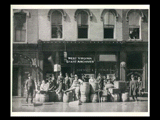 View of men at barrels in front of buildings during Wheeling flood. Signs include Devinney & Heinlein Proprietors, Harry Joyce's [Ca]fe, Belmont beer, Lemps beer.