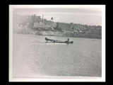 Wilma Swenson paddling a canoe on the Ohio River. Industrial complex buildings in the background.