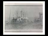 The Elm Grove railroad depot and crossing on dirt road. Sign for Pryor & Woods, hardware at right.